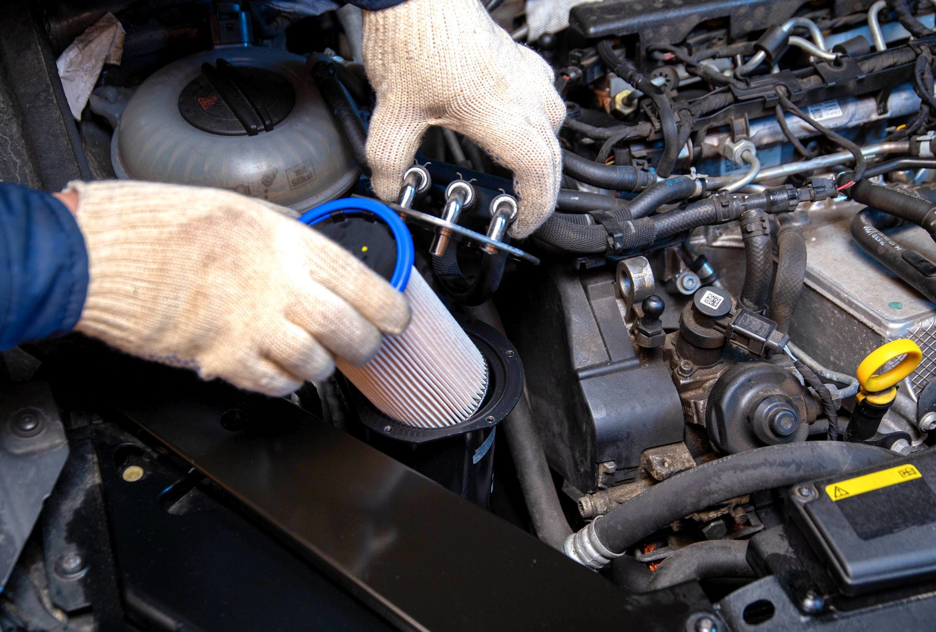 Hands in gloves replacing an air filter in a car engine.