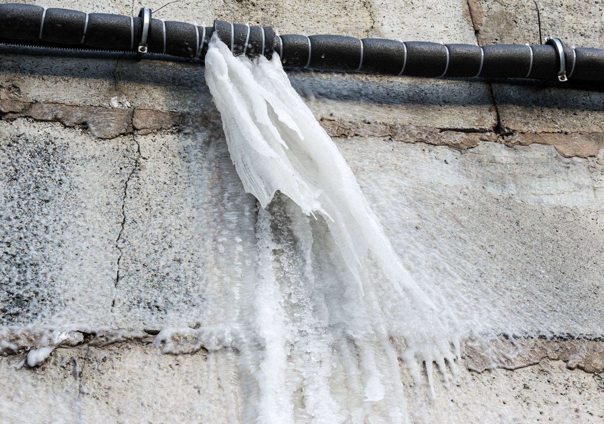 Water spilling from a black pipe onto a gray stone wall below.