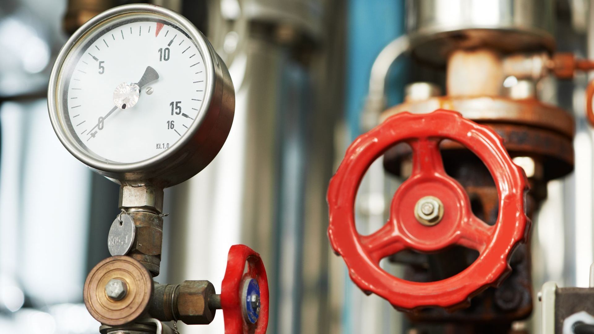 A close up of a pressure gauge and a red valve in a factory.