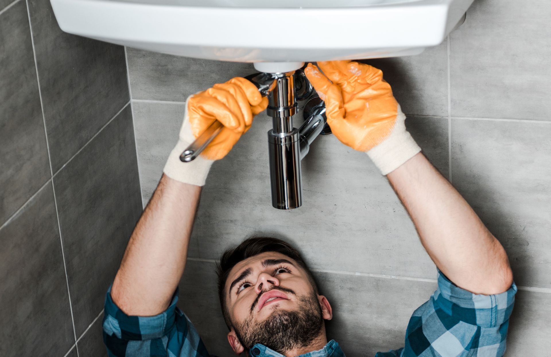 A man is fixing a sink in a bathroom with a wrench.