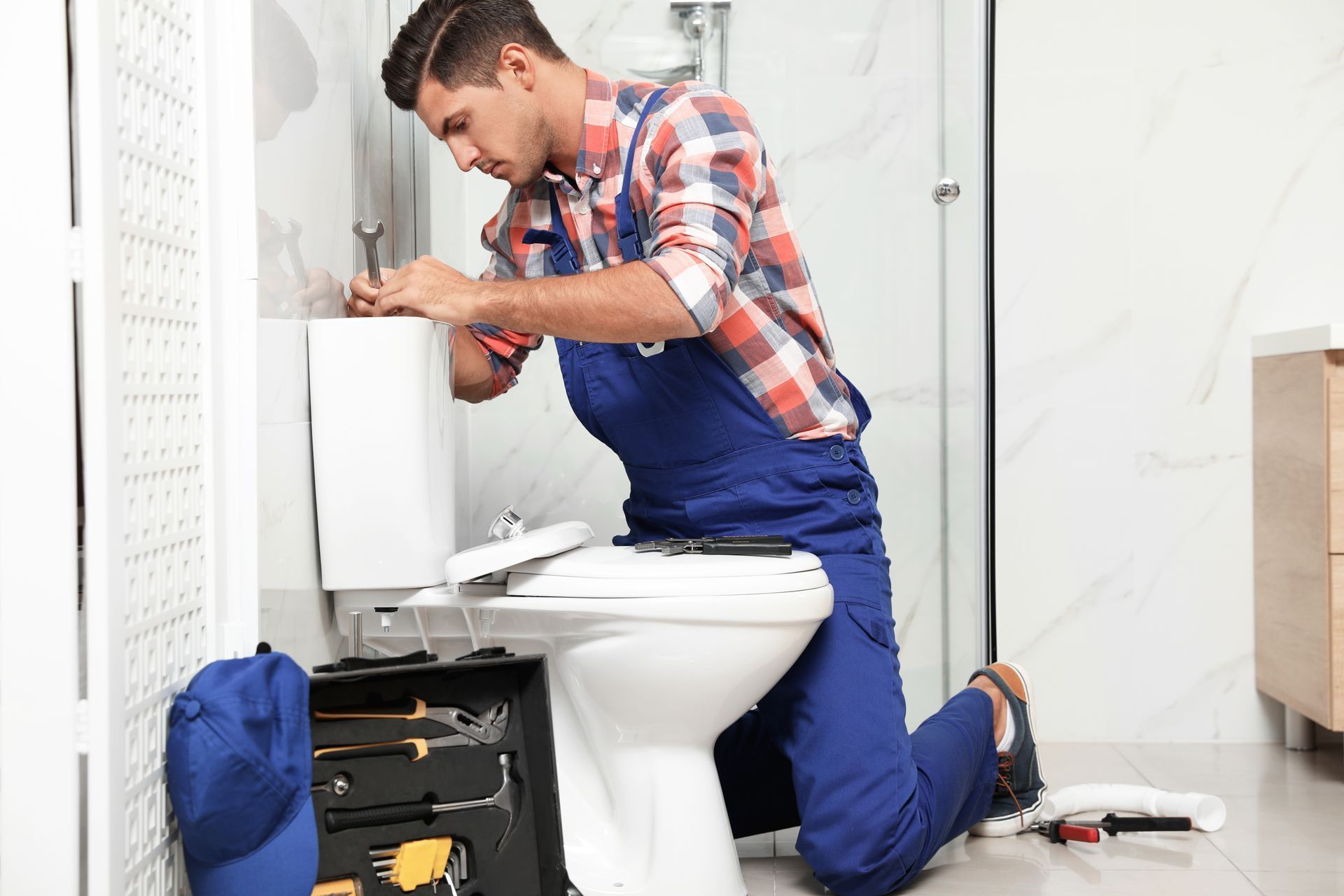 A plumber is fixing a toilet in a bathroom.