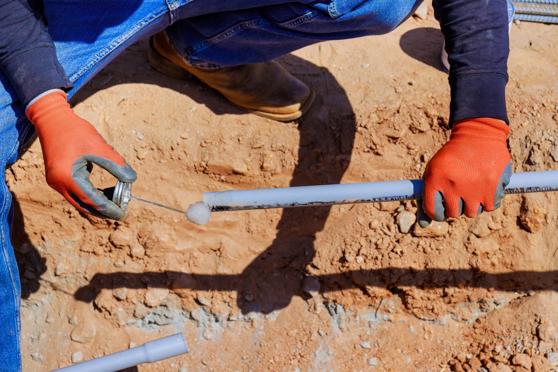 A man wearing orange gloves is working on a pipe in the dirt.