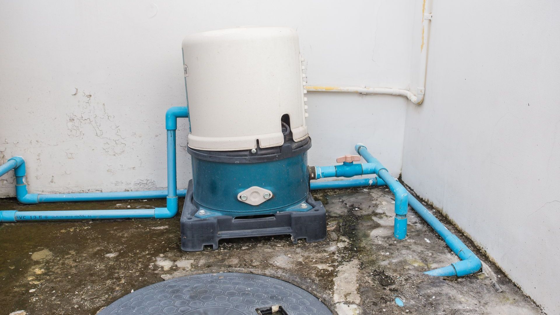 A water pump is sitting in a corner of a room next to a wall.