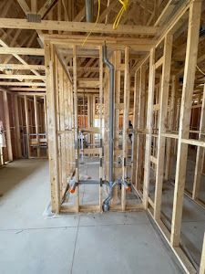 Wooden framing of a bathroom with installed plumbing pipes. Studs, concrete floor, and yellow wiring are also visible.