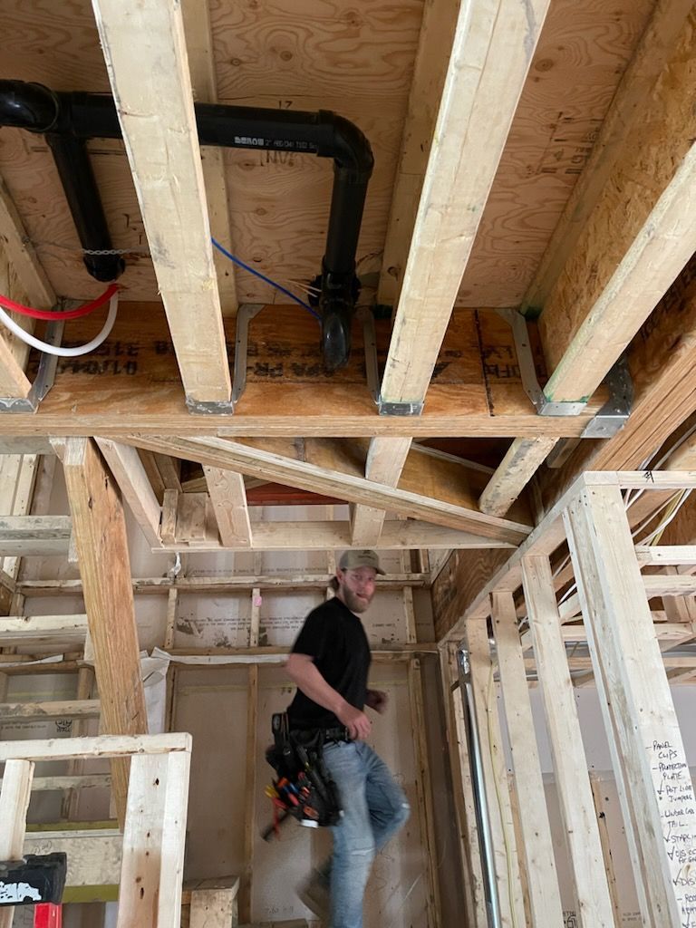 Man in a construction site looking at the camera, wood frame beams, plumbing visible.