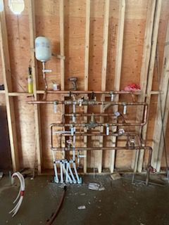 Copper plumbing system installed on wooden framing. A white expansion tank is mounted above.