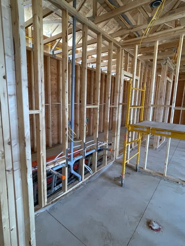Interior framing with plumbing pipes, electrical wires, and a yellow scaffolding.