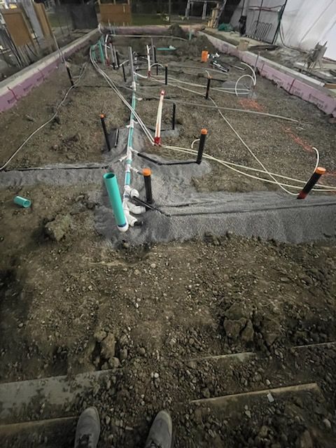 Construction site: plumbing pipes, concrete, and electrical wires laid in dirt, ready for a foundation pour.