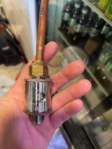 Hand holding a disassembled chrome and brass faucet component with copper pipe.