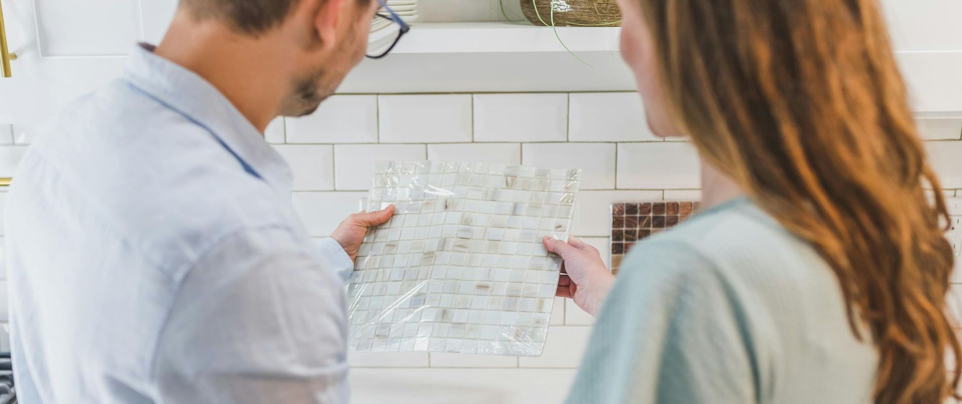 A man and a woman are looking at a piece of tile in a kitchen.