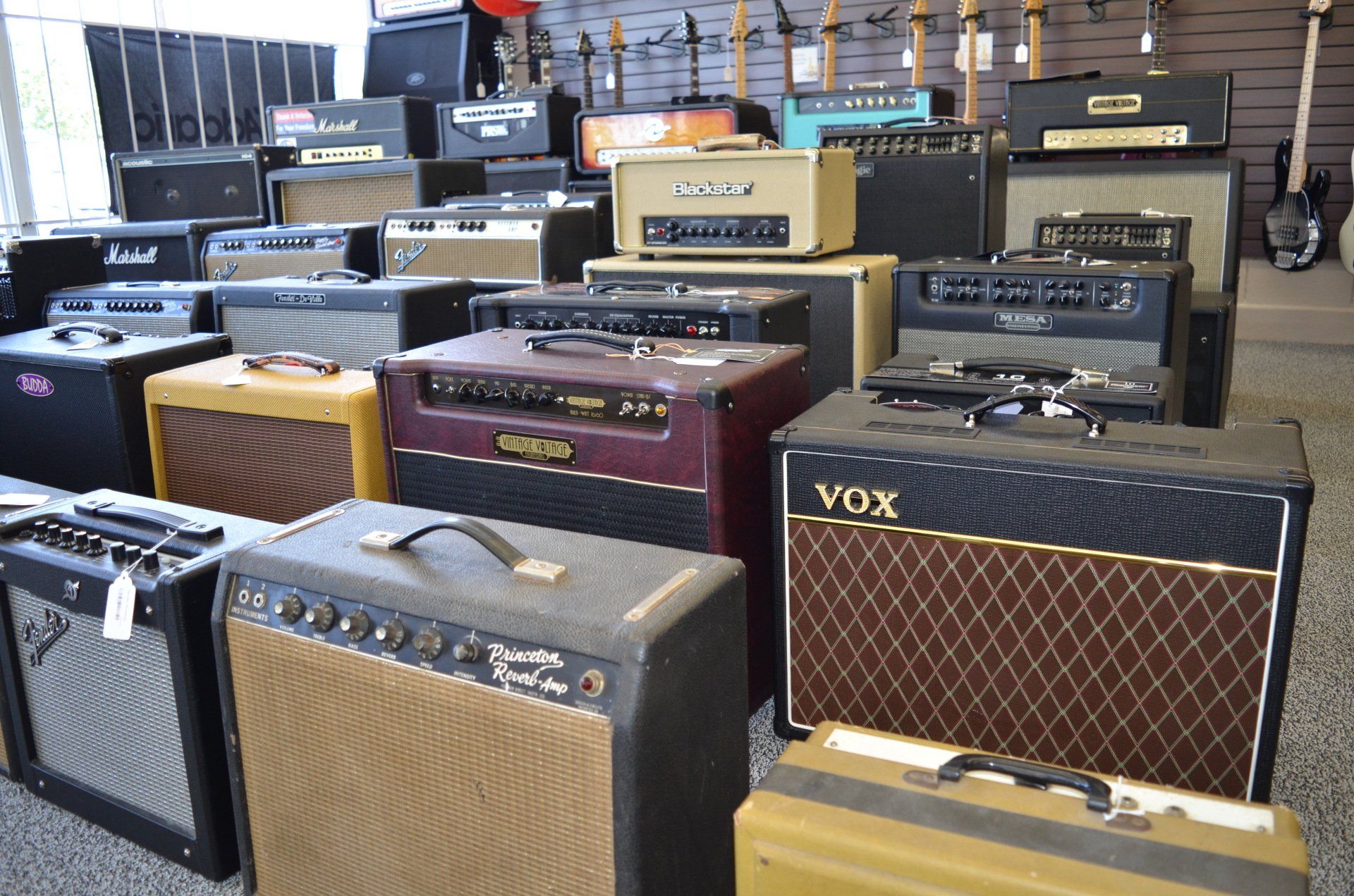 Many guitar amplifiers stacked in a music store, including Vox, Marshall, and Fender brands.