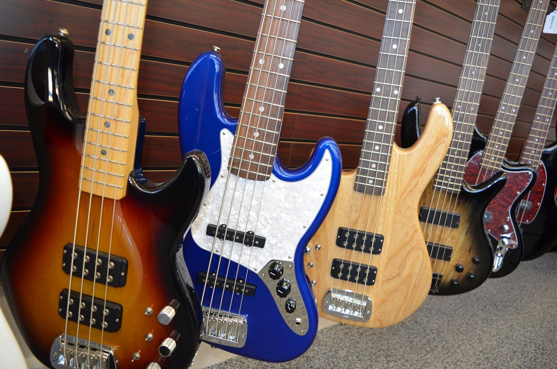 Row of colorful electric bass guitars leaning against a brown wall.