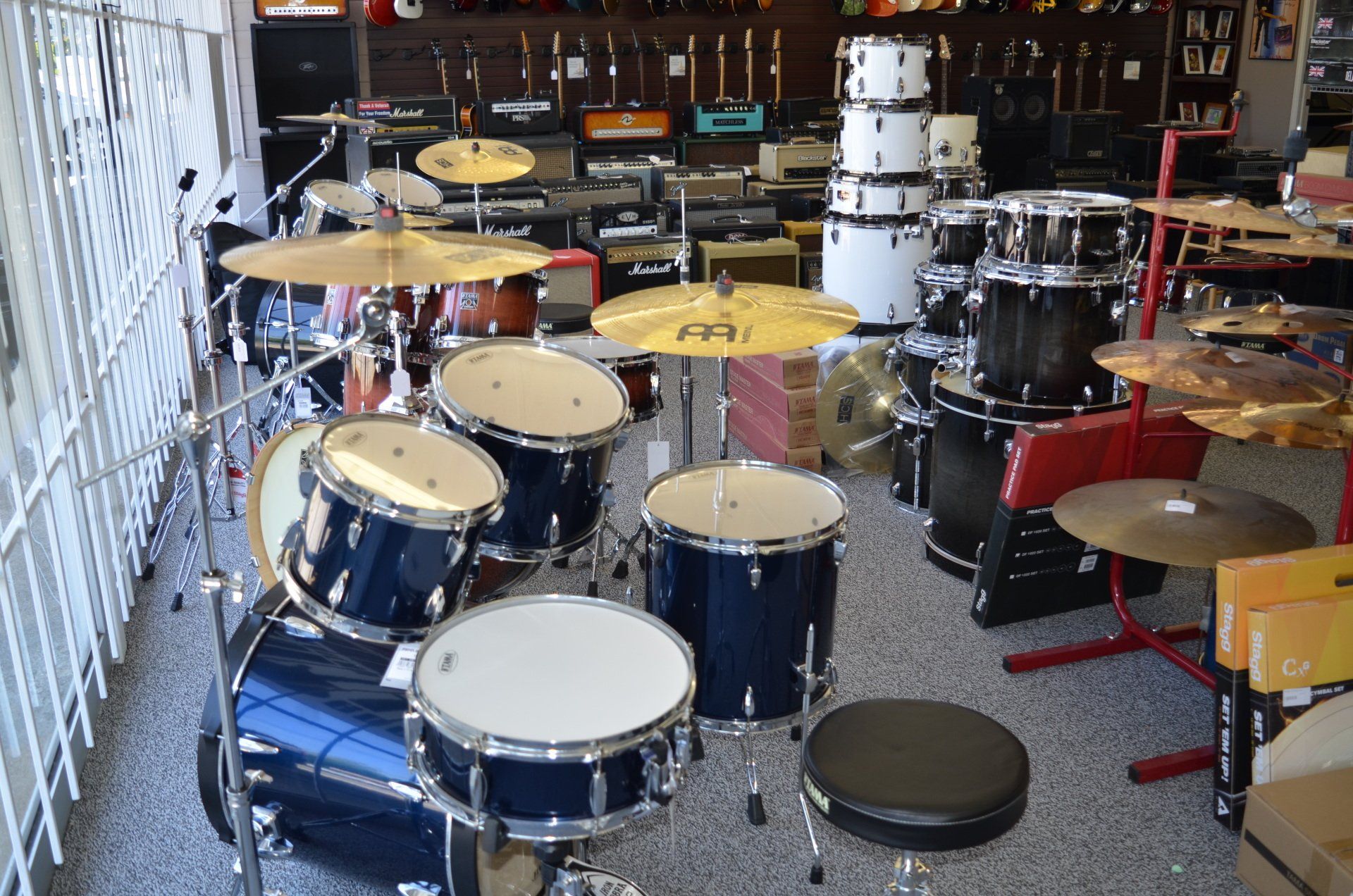 Drum sets on display in a music store, including blue and white sets, cymbals, and equipment.