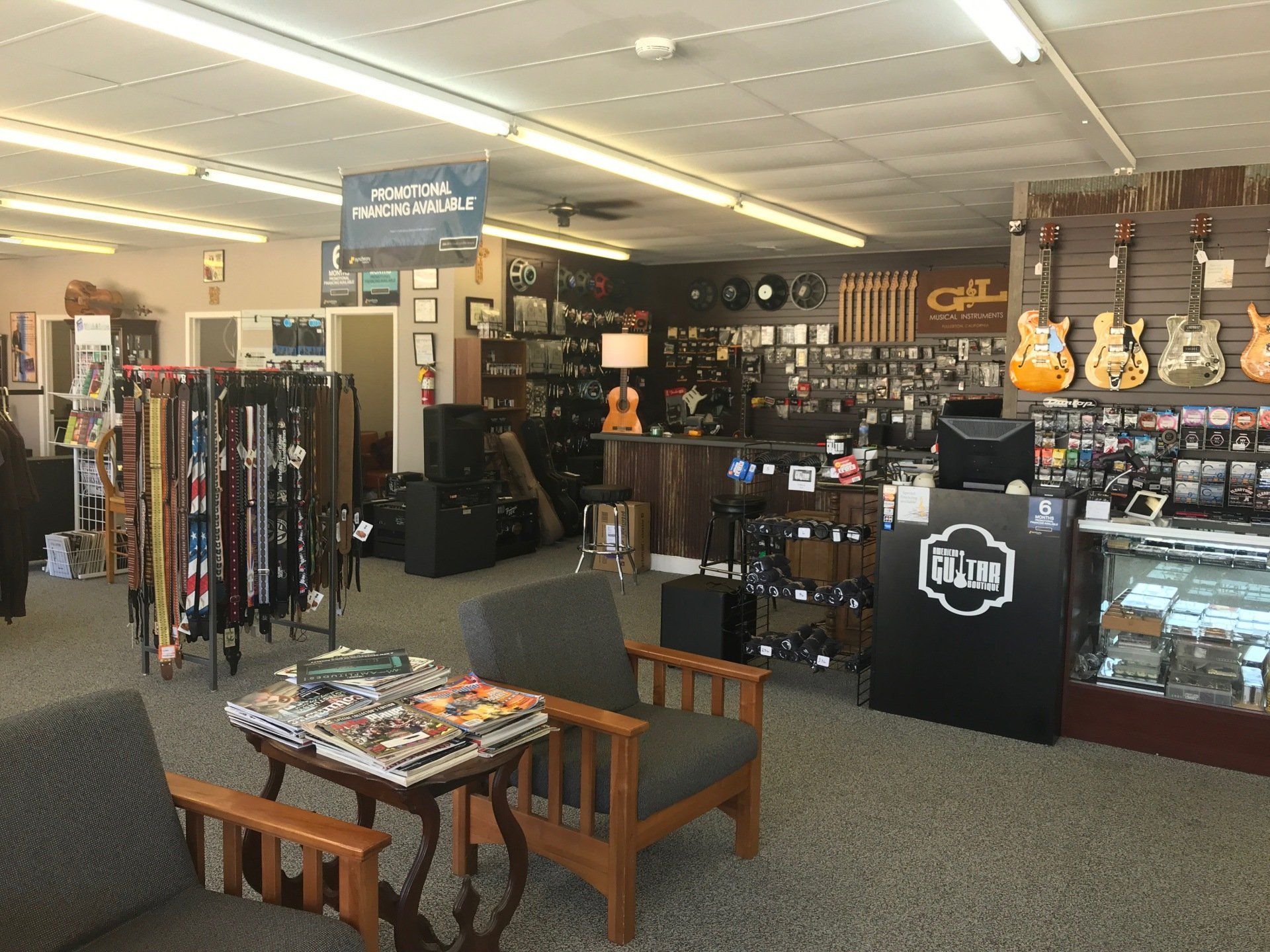 Interior of a music store; guitars, amplifiers, and accessories on display. Two armchairs and small table in the foreground.