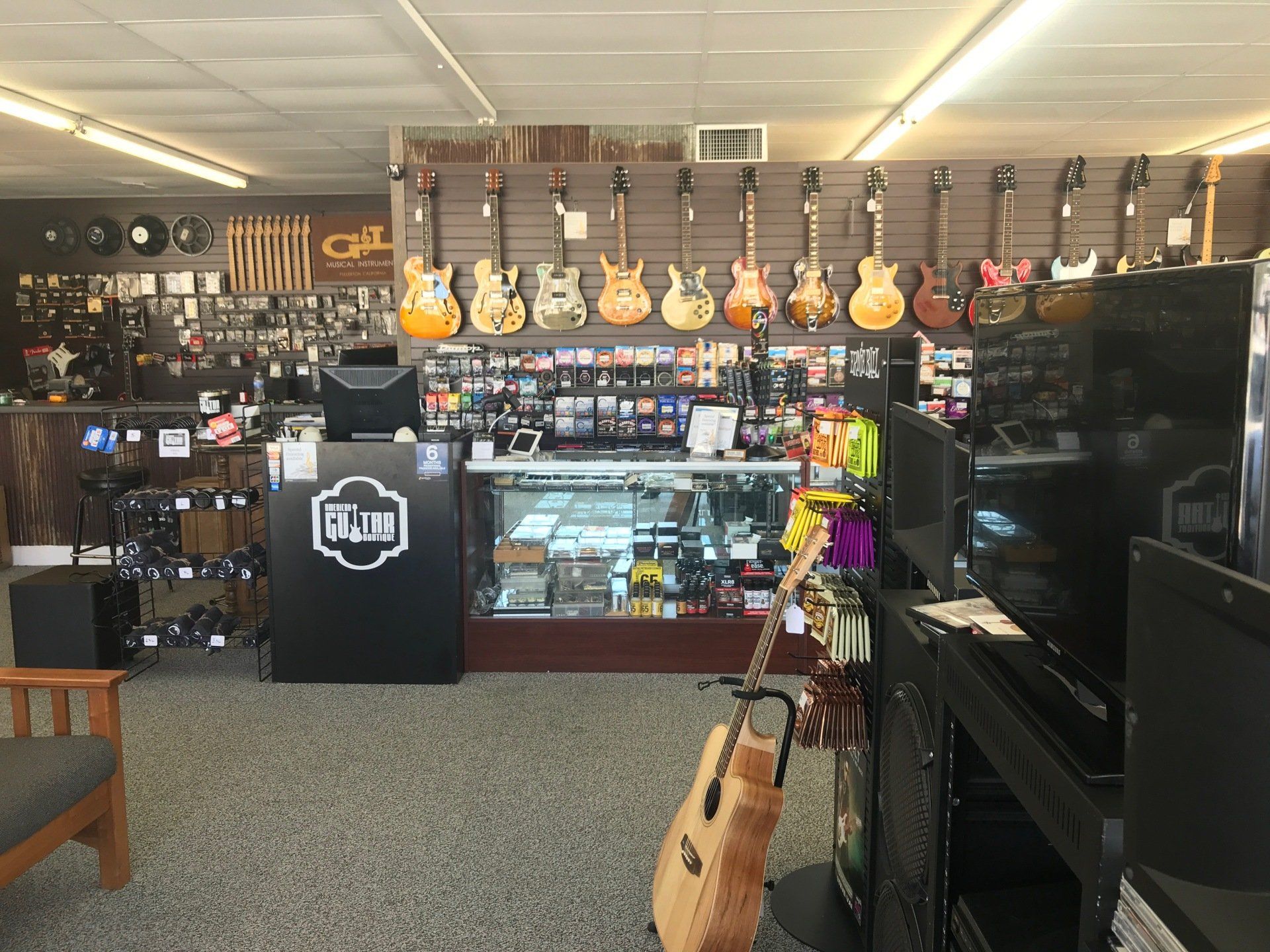 Music store interior, guitars hanging on wall, counter with logo, shelves of equipment.