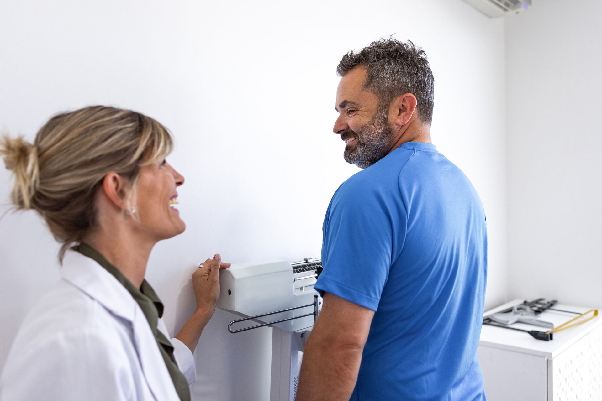 A doctor is talking to a patient who is standing in front of a scale.