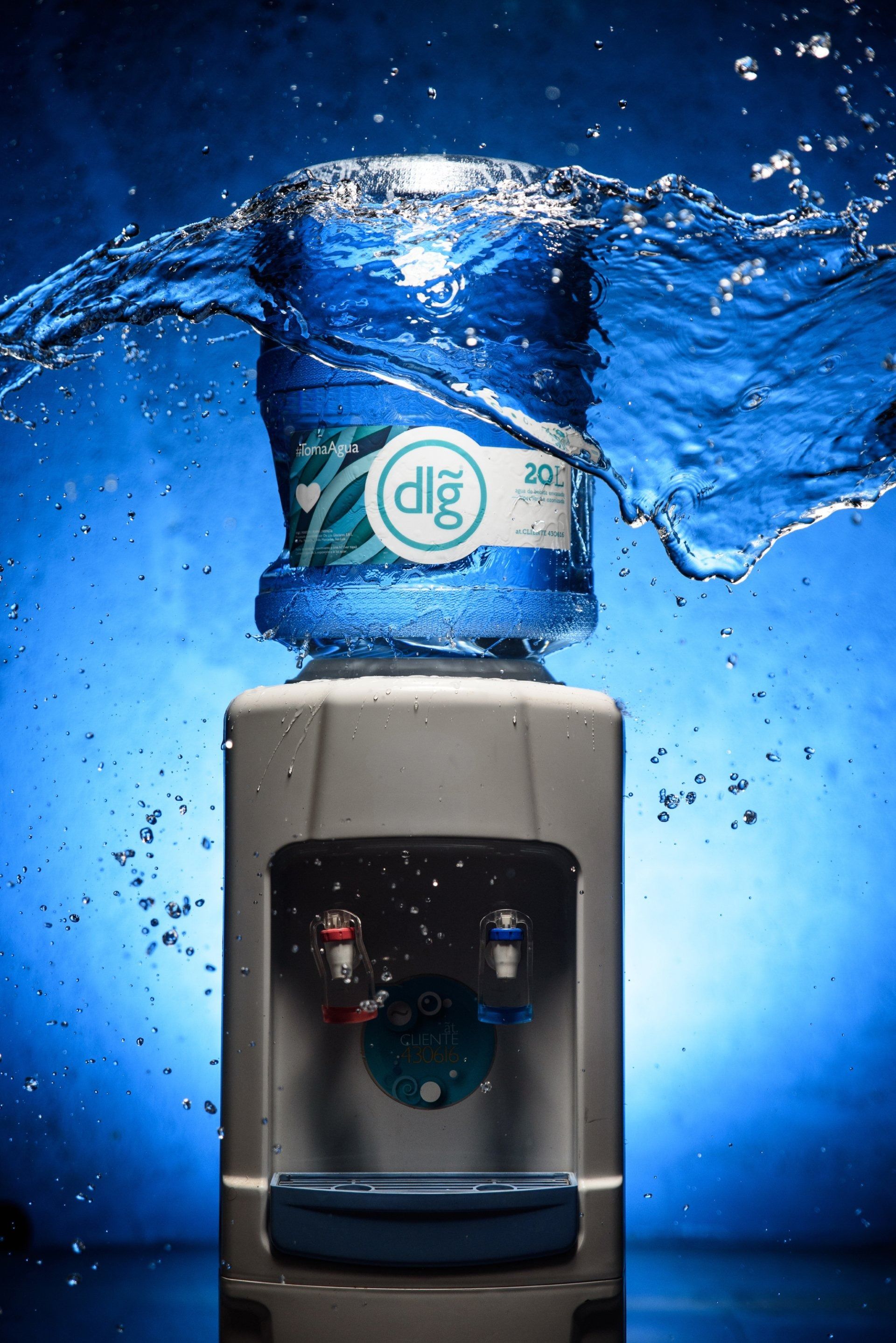 Dispensador de agua con una botella azul que salpica agua sobre un fondo azul brillante.