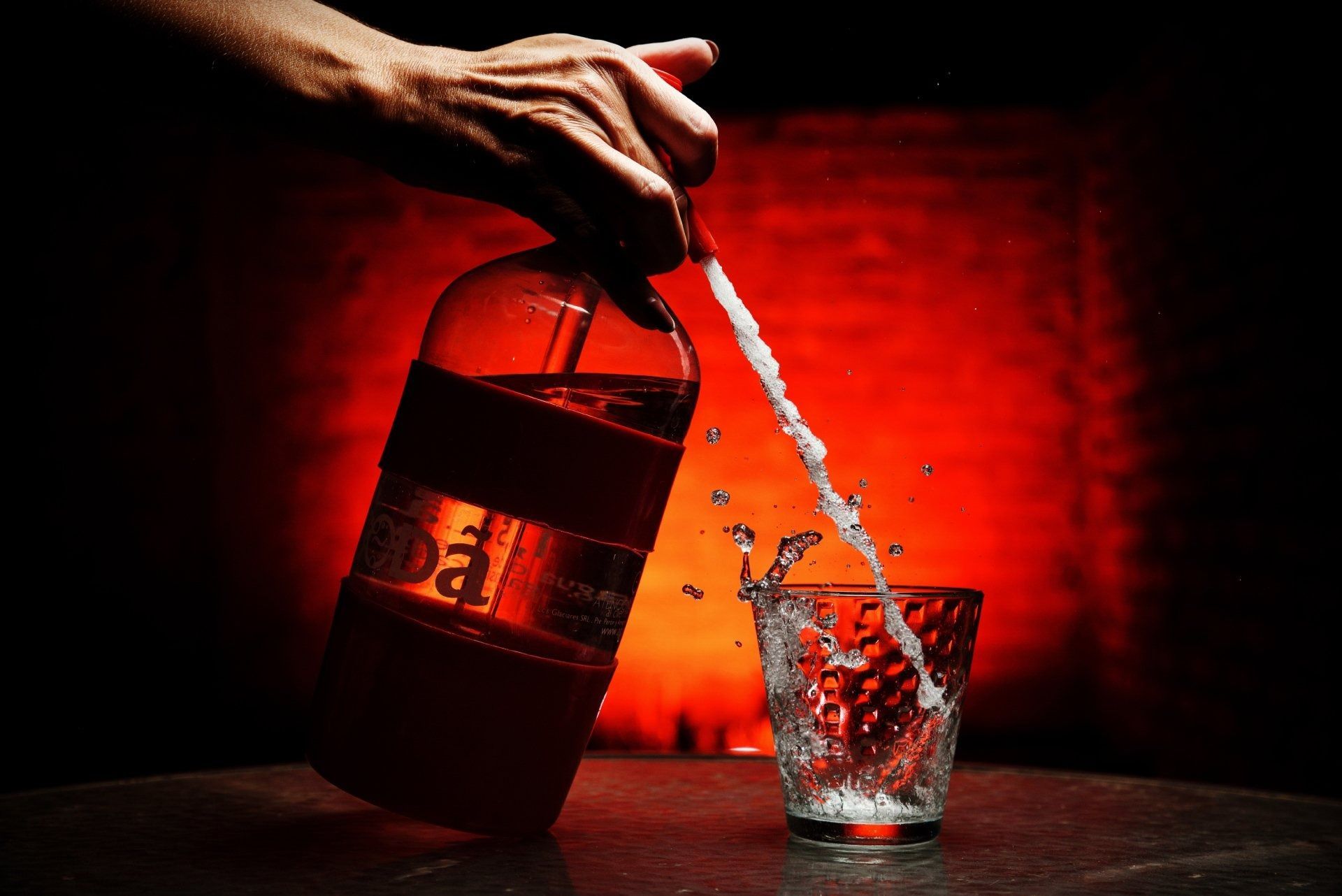 Verter licor a mano de una botella en un vaso sobre una mesa con fondo rojo.