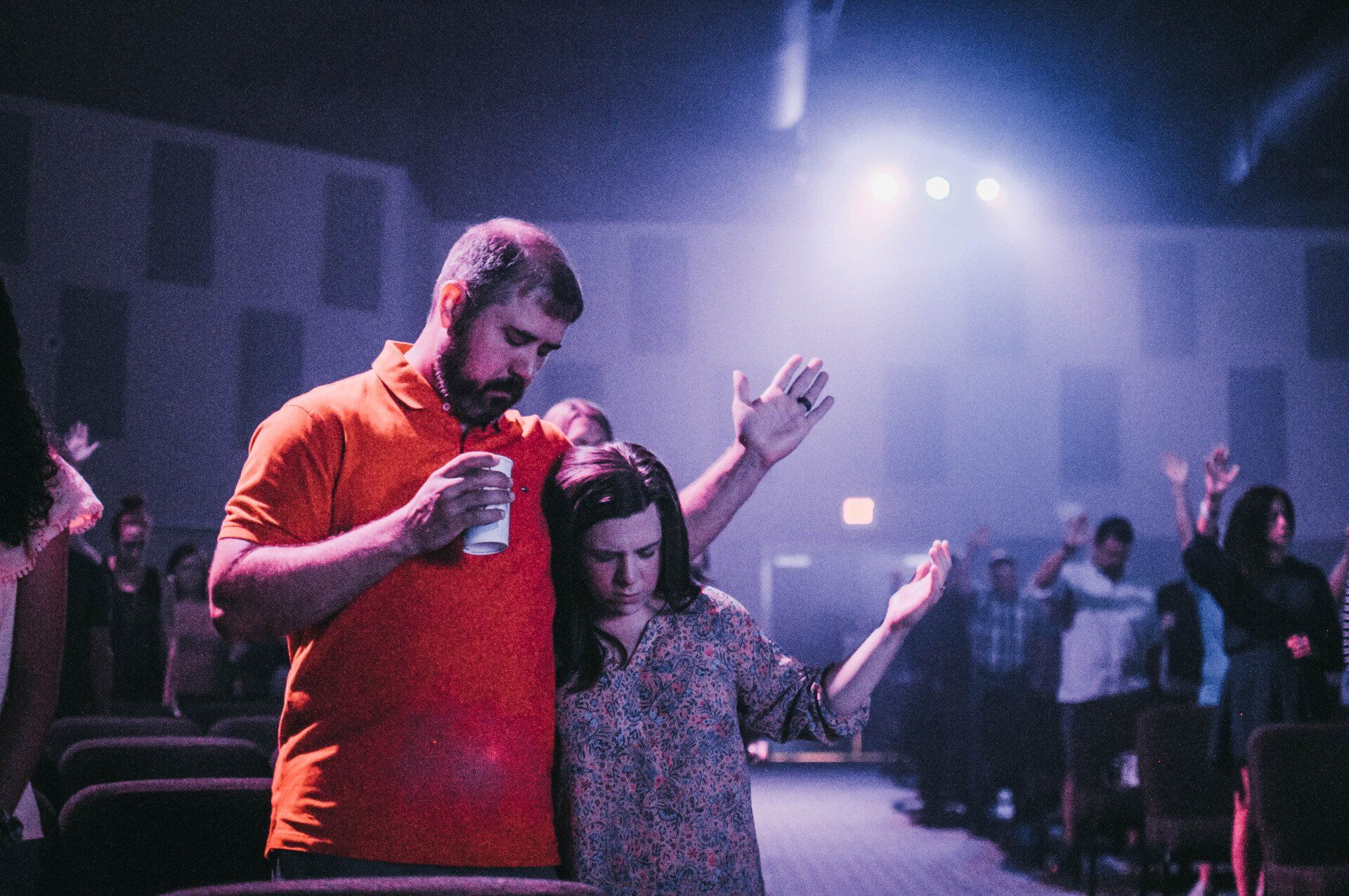A man and a woman are standing next to each other in a dark room with their arms in the air.