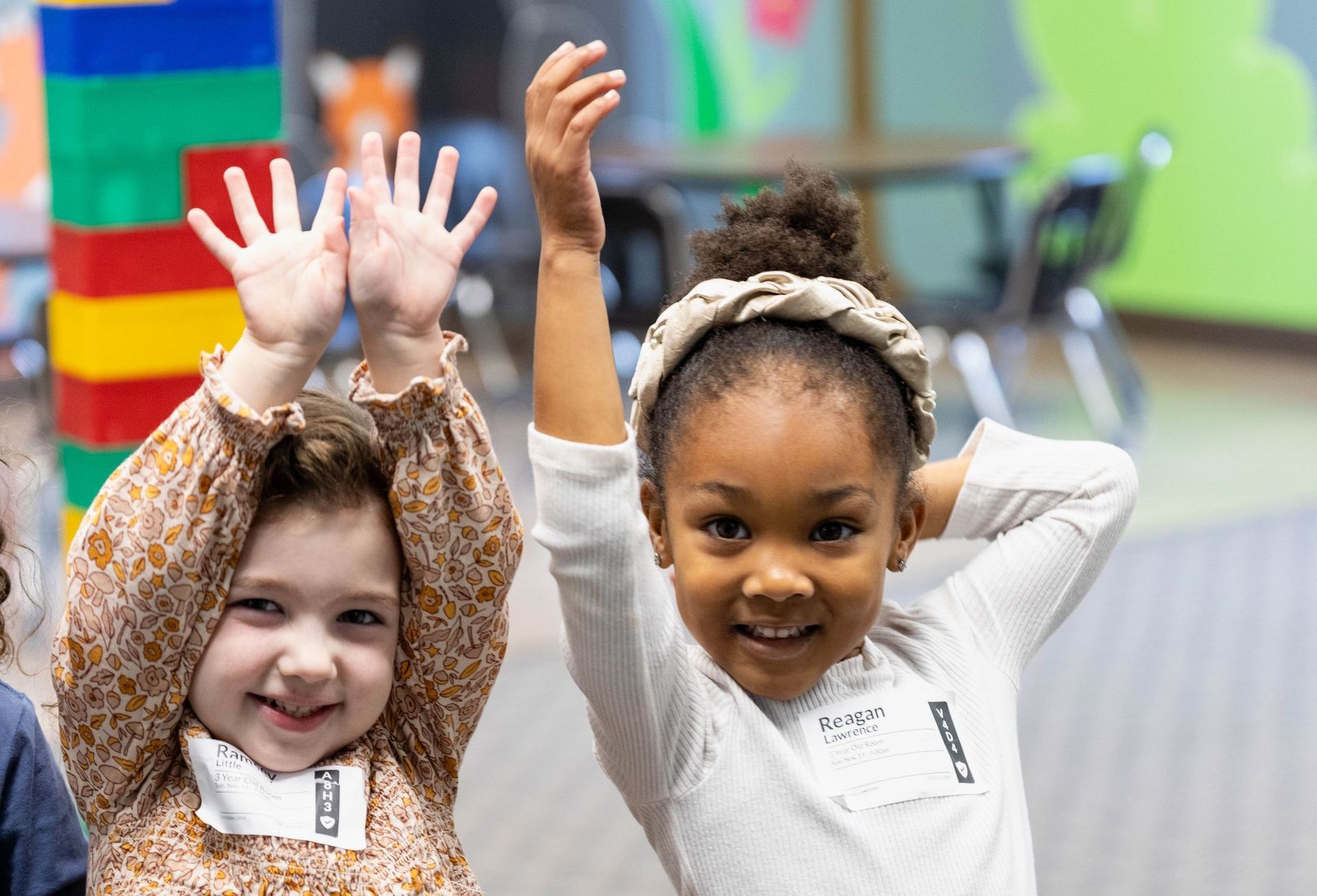 Two little girls are raising their hands in the air.