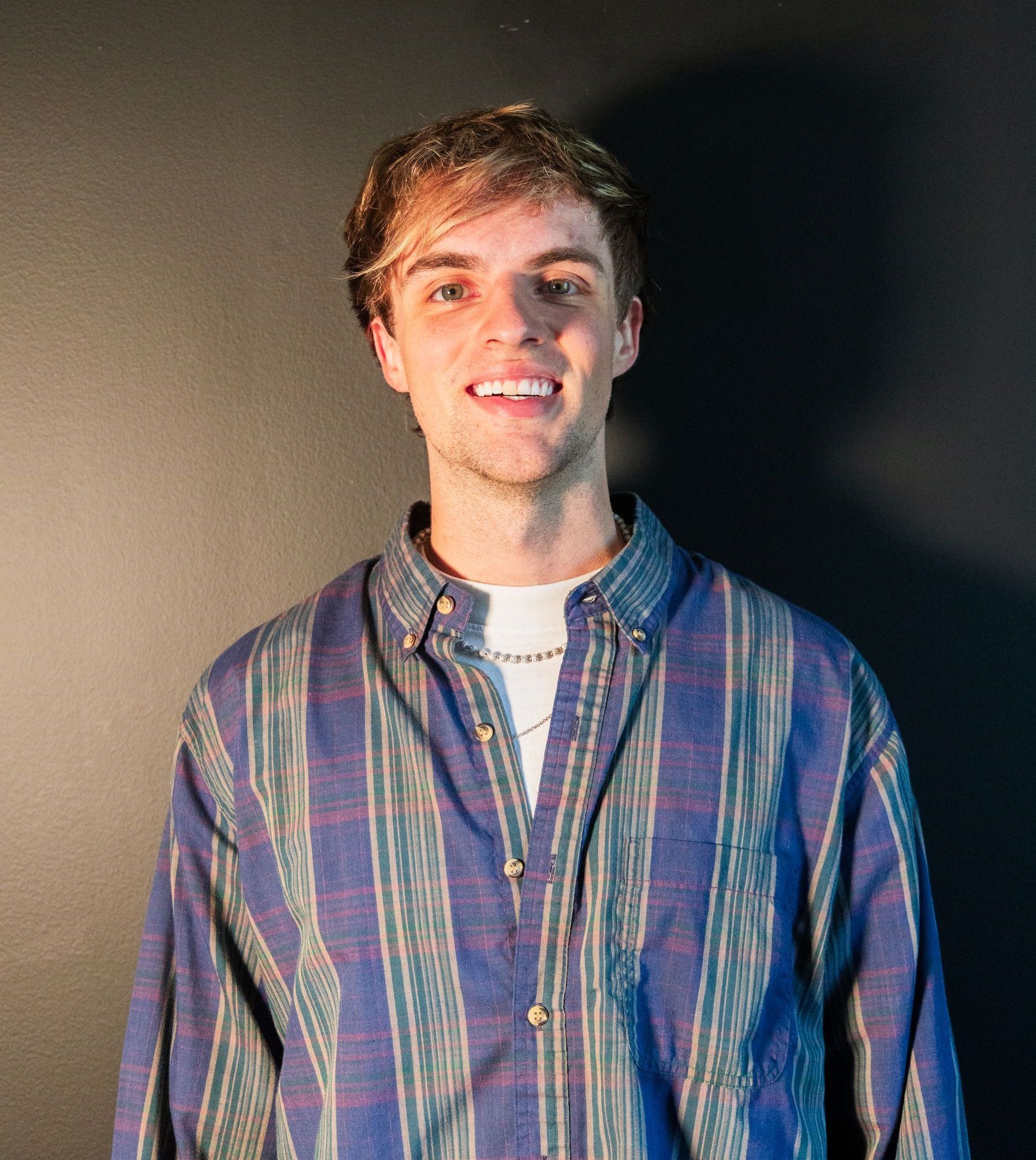 A young man wearing a striped shirt is smiling for the camera.