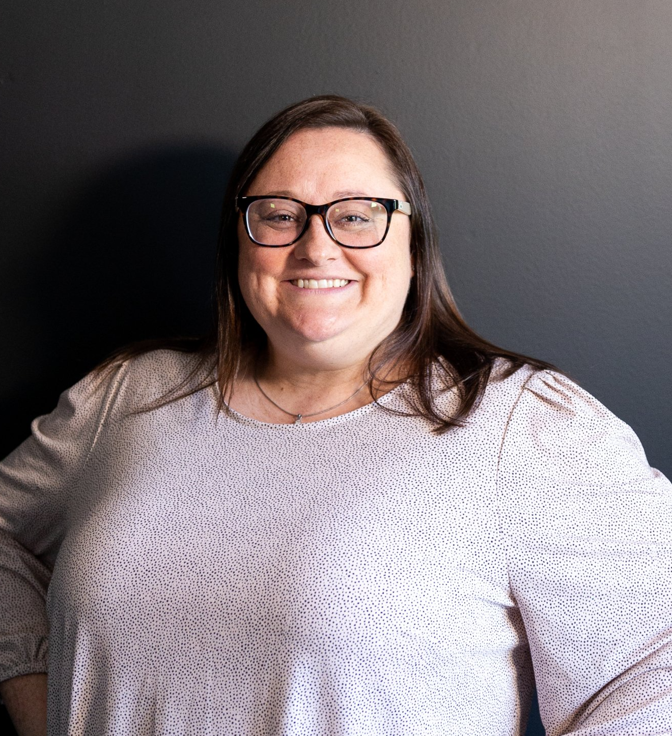 A woman wearing glasses and a white shirt is smiling for the camera.