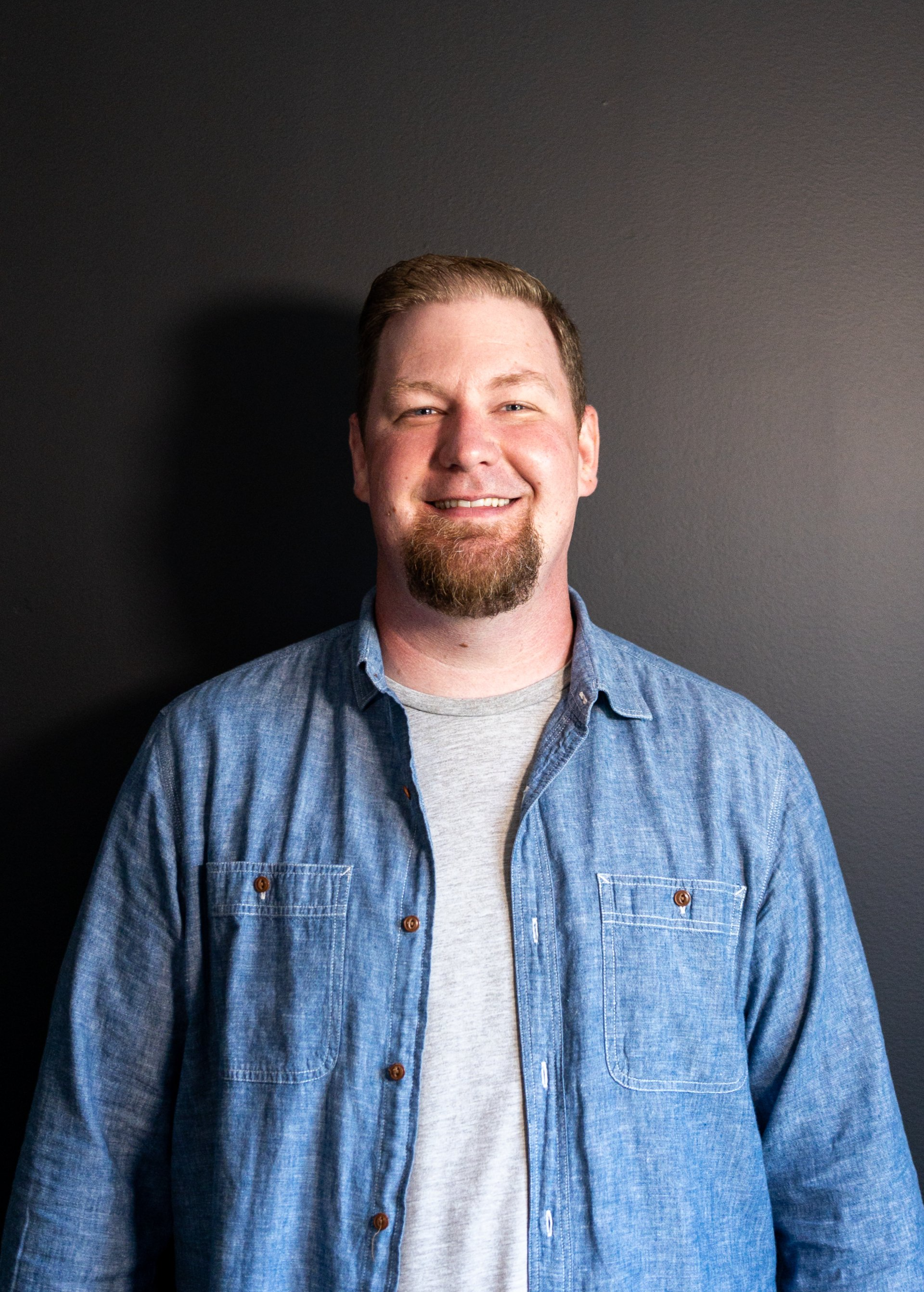 A man with a beard is wearing a blue shirt and smiling.