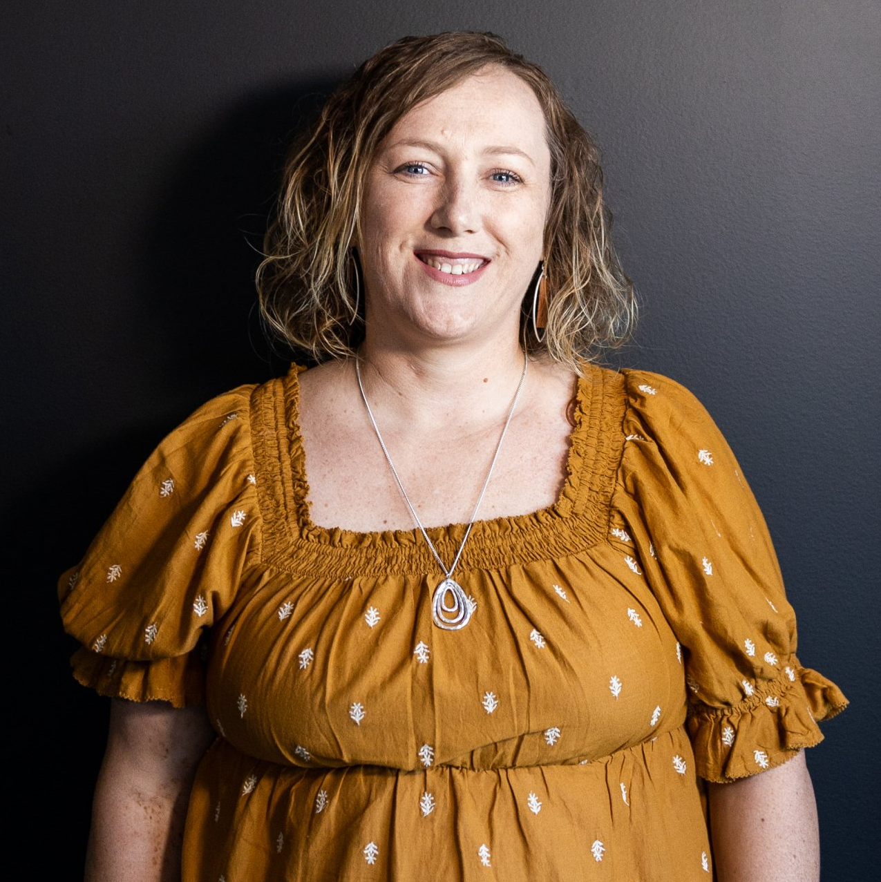 A woman in a yellow dress is smiling and wearing a necklace.