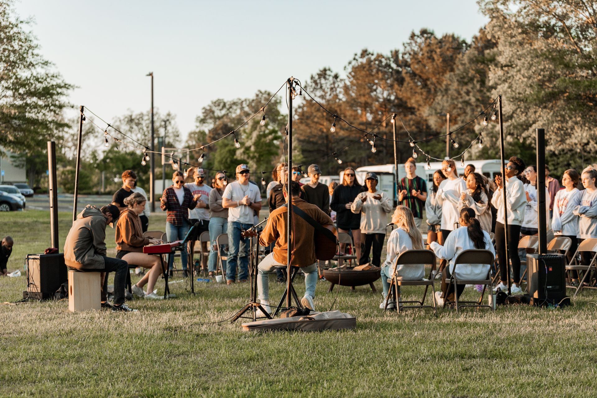 A man is playing a guitar in front of a crowd of people in a park.