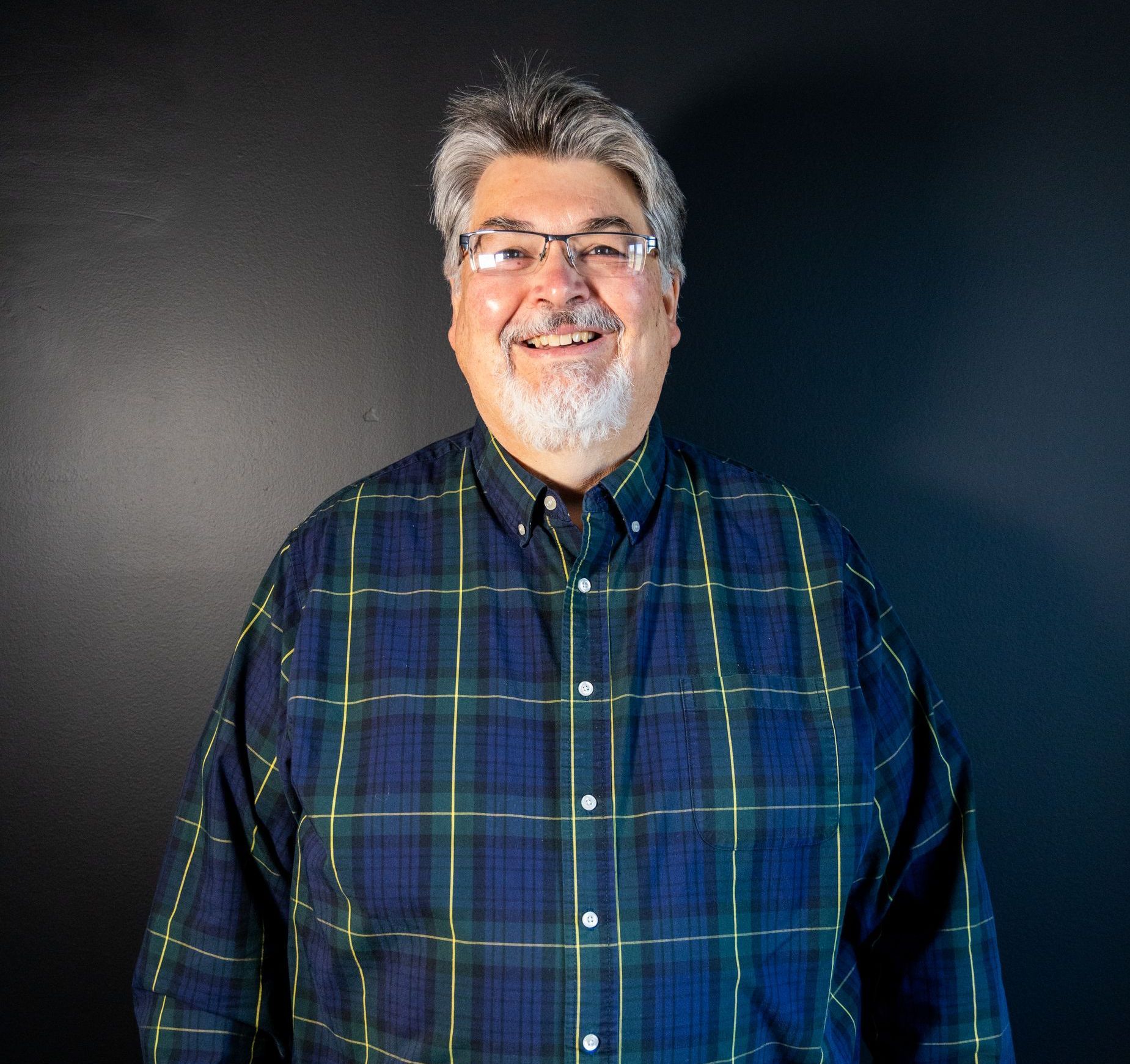 A man wearing glasses and a plaid shirt is smiling for the camera.