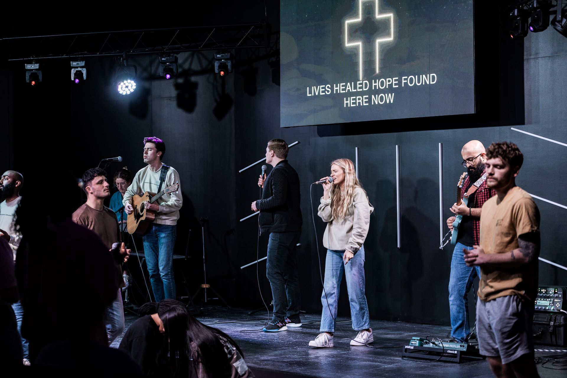 A group of people are standing on a stage singing into microphones.