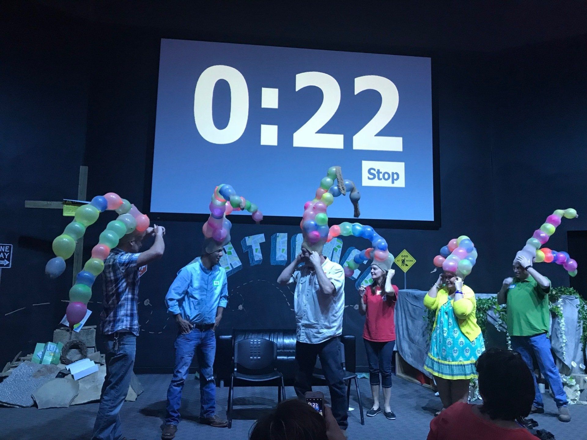 A group of people are playing with balloons in front of a screen that says 2:22