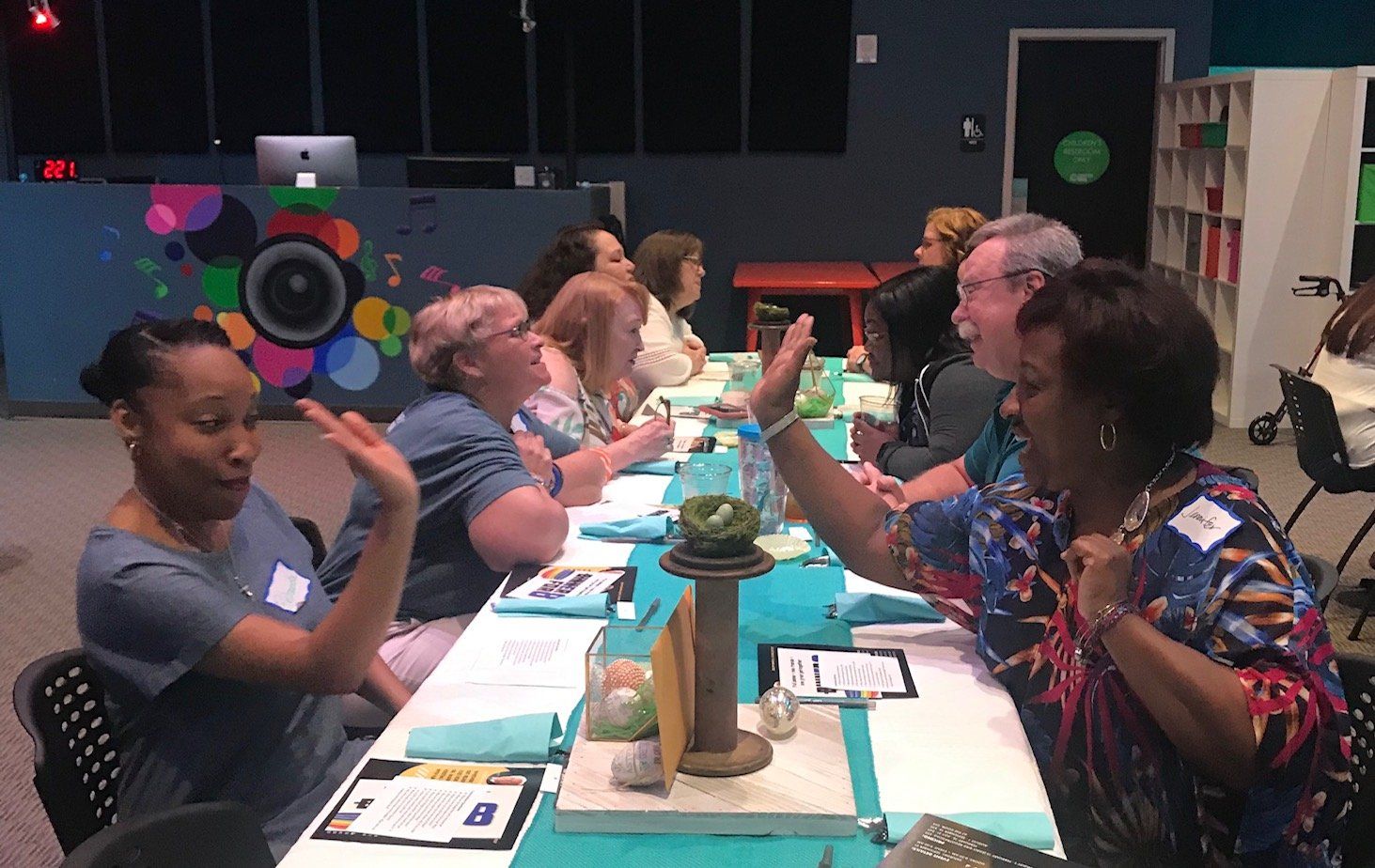 A group of people are sitting at a long table with their hands in the air.