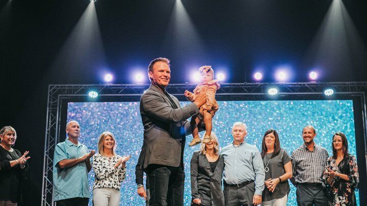 A man is holding a baby on a stage in front of a crowd of people.
