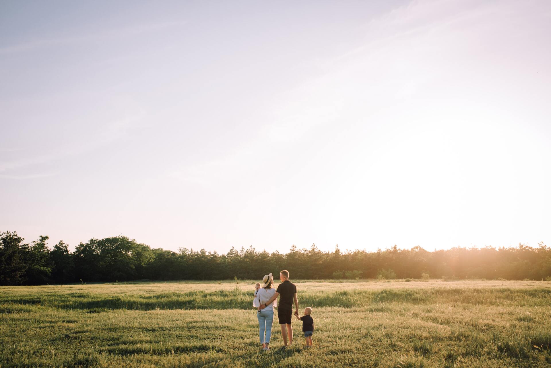 A family is walking through a grassy field at sunset.