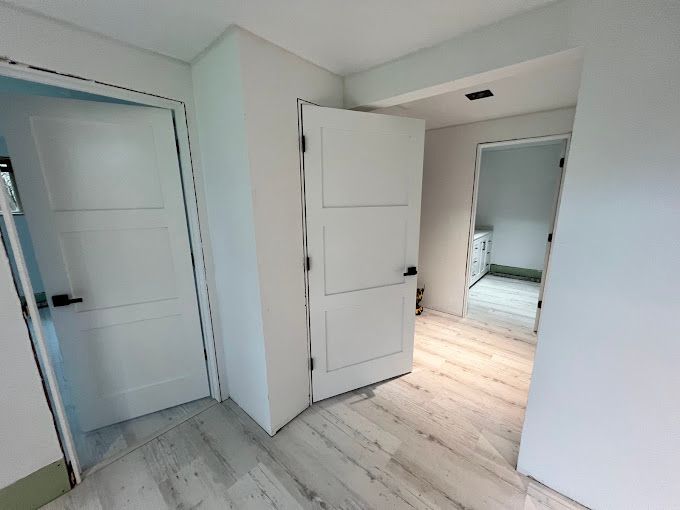 A hallway with white doors and wooden floors leading to a bathroom.