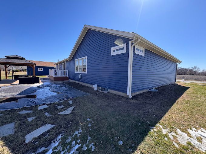 A blue house with white siding is sitting in the middle of a grassy field.