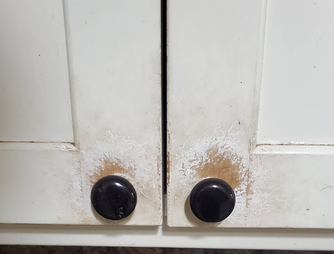 Two white cabinet doors with worn paint showing wood underneath around the black circular knobs.