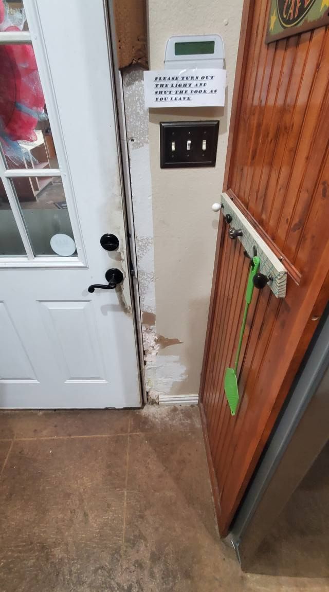 A white door, a wall switch panel, a thermostat, and a wooden rack with a green utensil inside a home.