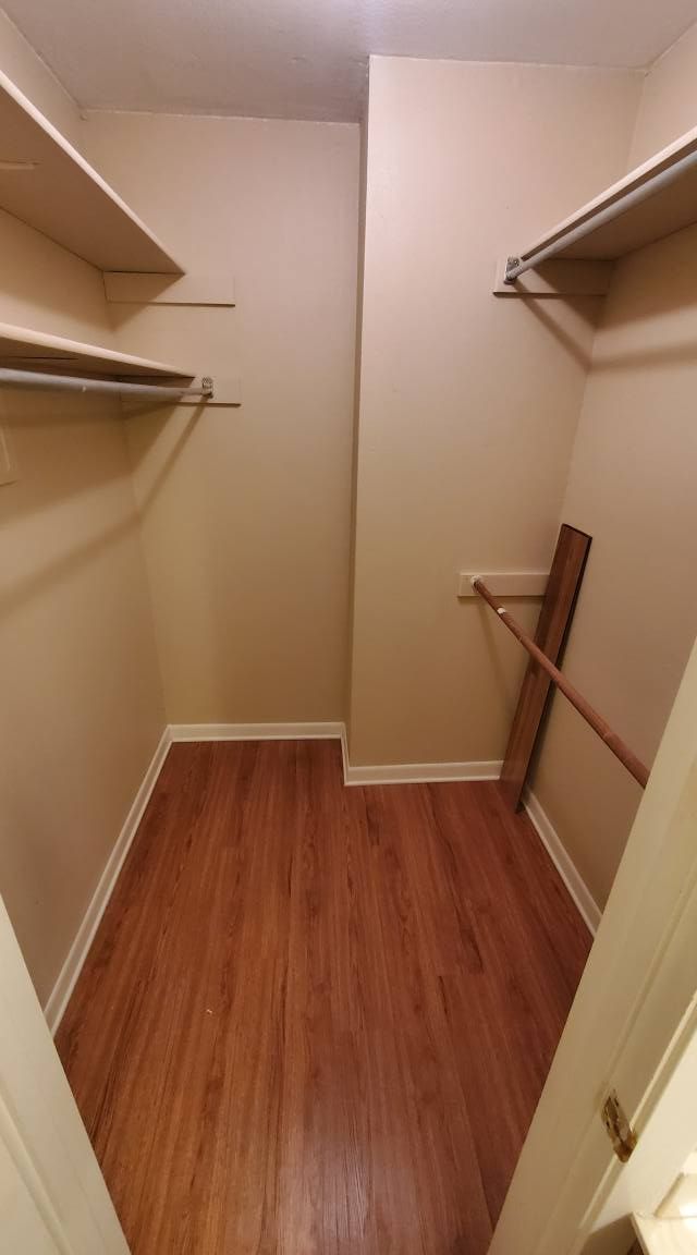 An empty walk-in closet with beige walls, wood-look flooring, and white shelving units on the left and right walls.