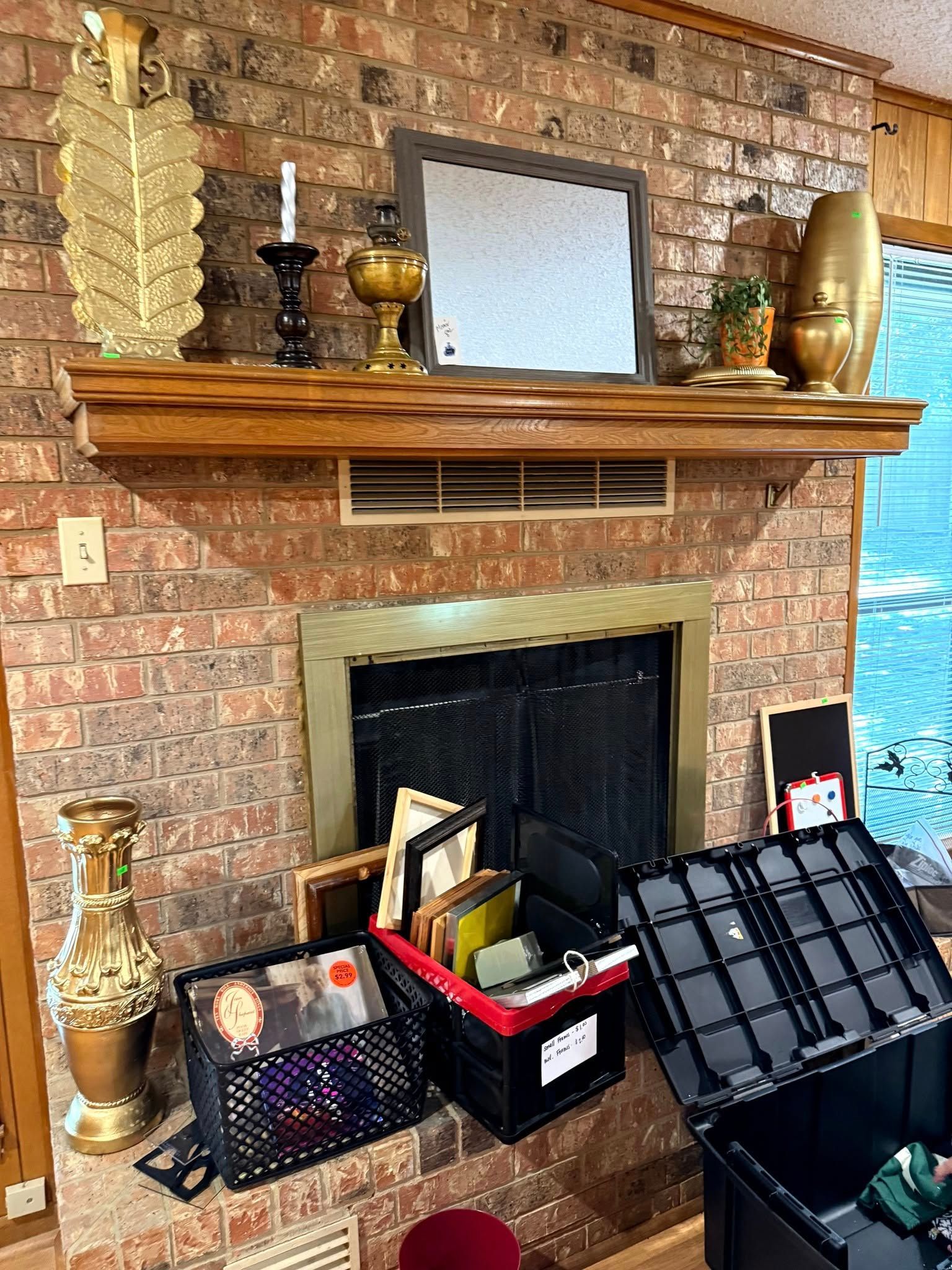 A fireplace with a brick surround, wooden mantel, decorative objects, and boxes of books and items on the hearth.