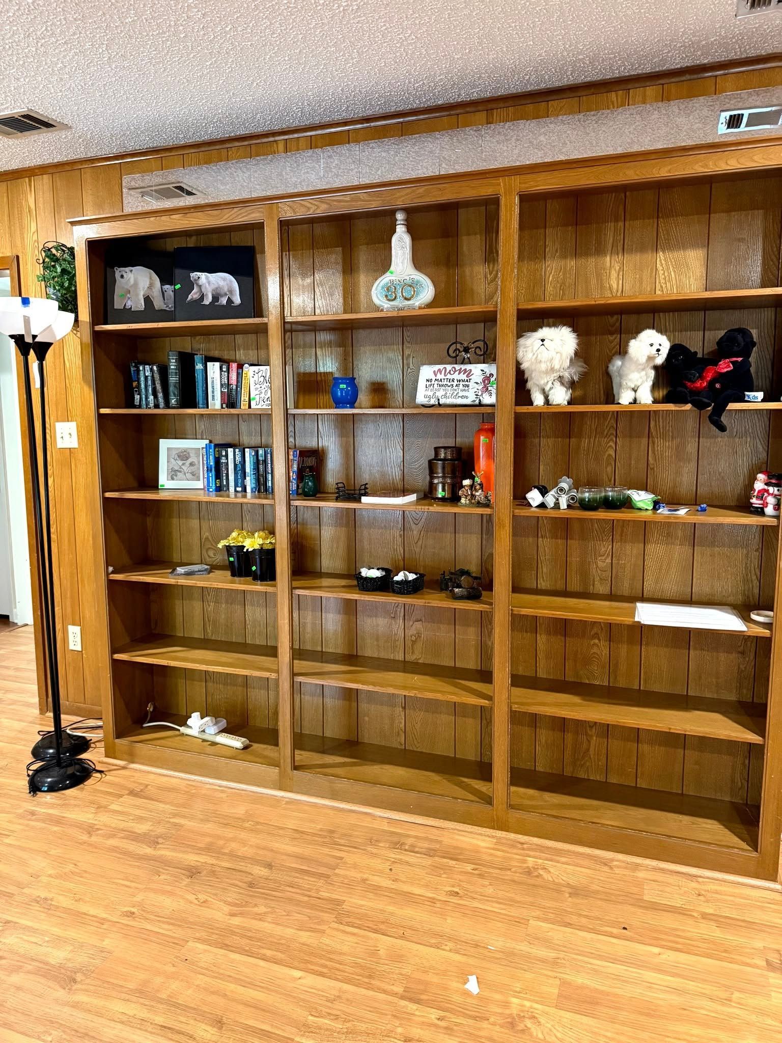 A large, three-section oak bookshelf filled with books, small decorative objects, and several plush animal toys.