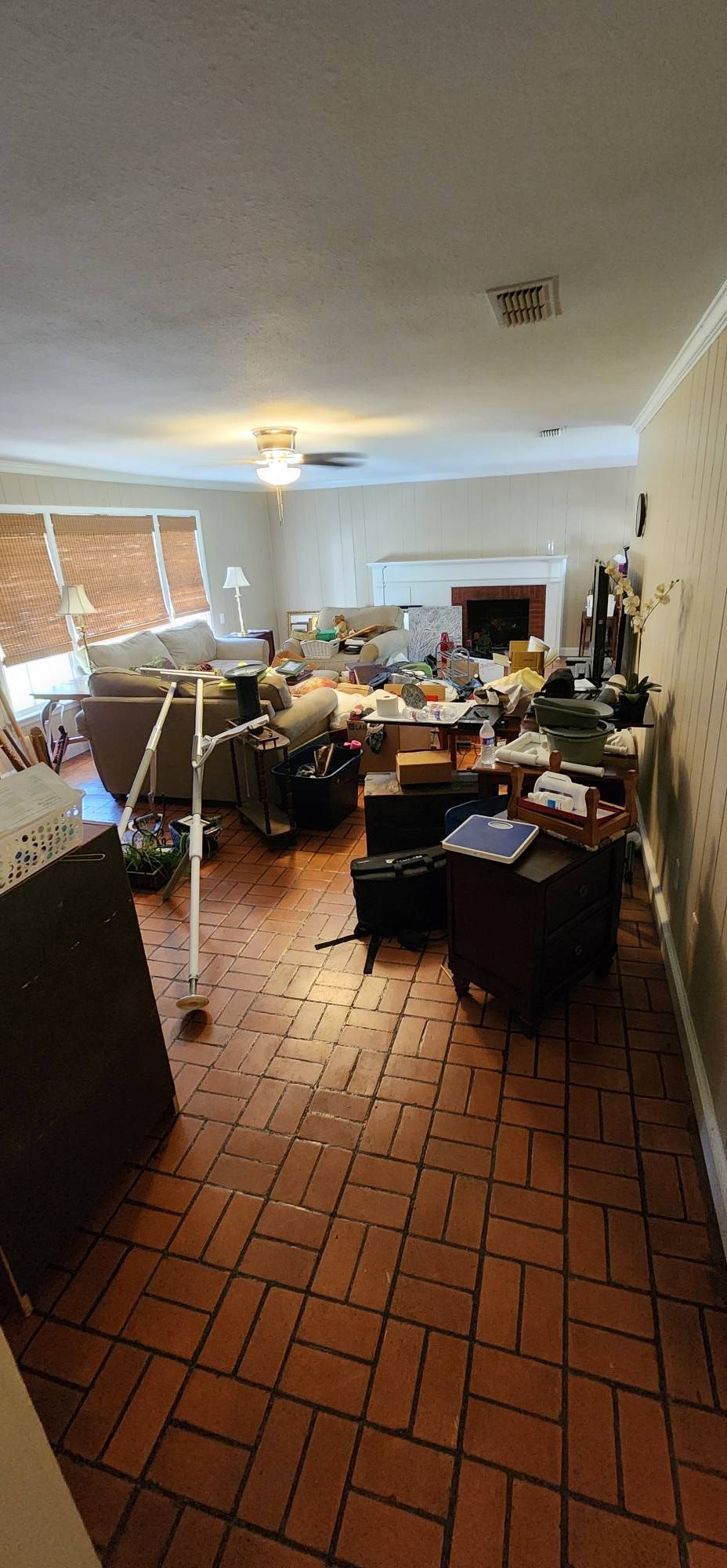 A living room with terracotta-colored brick flooring, a couch, a fireplace, and various scattered household items.