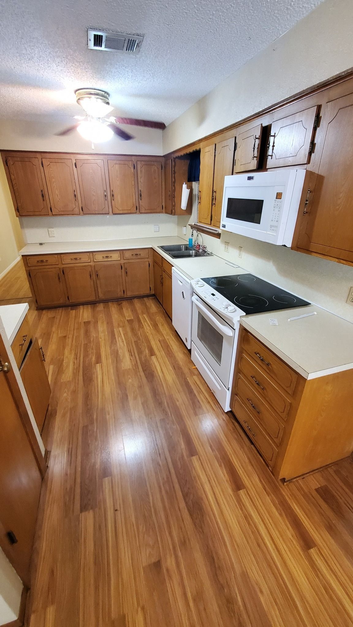 A kitchen with wooden cabinets, light countertops, a white oven, a microwave, and hardwood flooring.