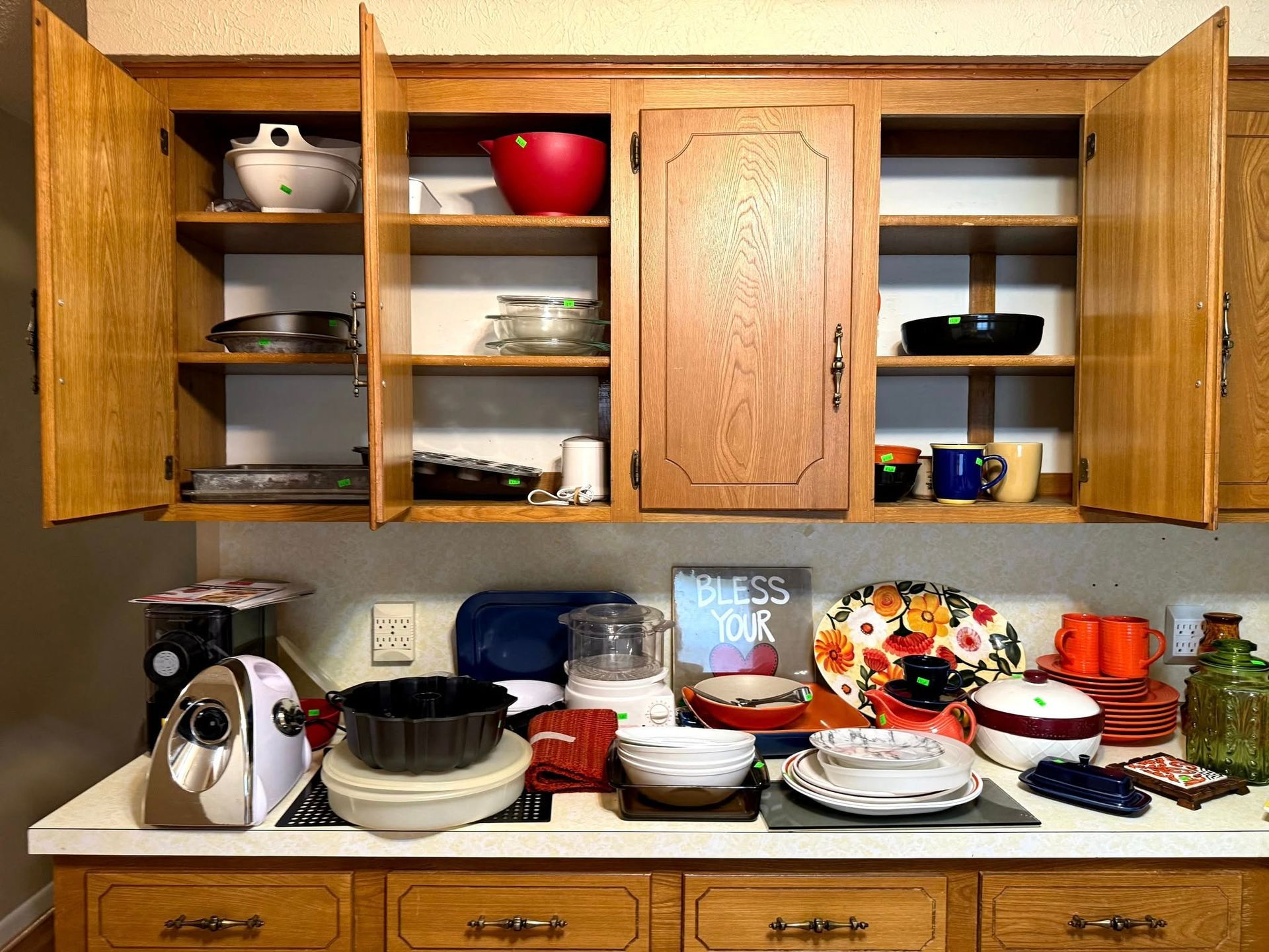 Open oak kitchen cabinets above a counter cluttered with bowls, kitchen gadgets, dishes, and a 
