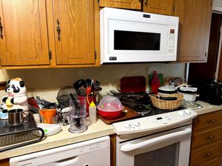 A cluttered kitchen counter with a stove, white microwave, cabinets, a panda cookie jar, and various kitchen tools.