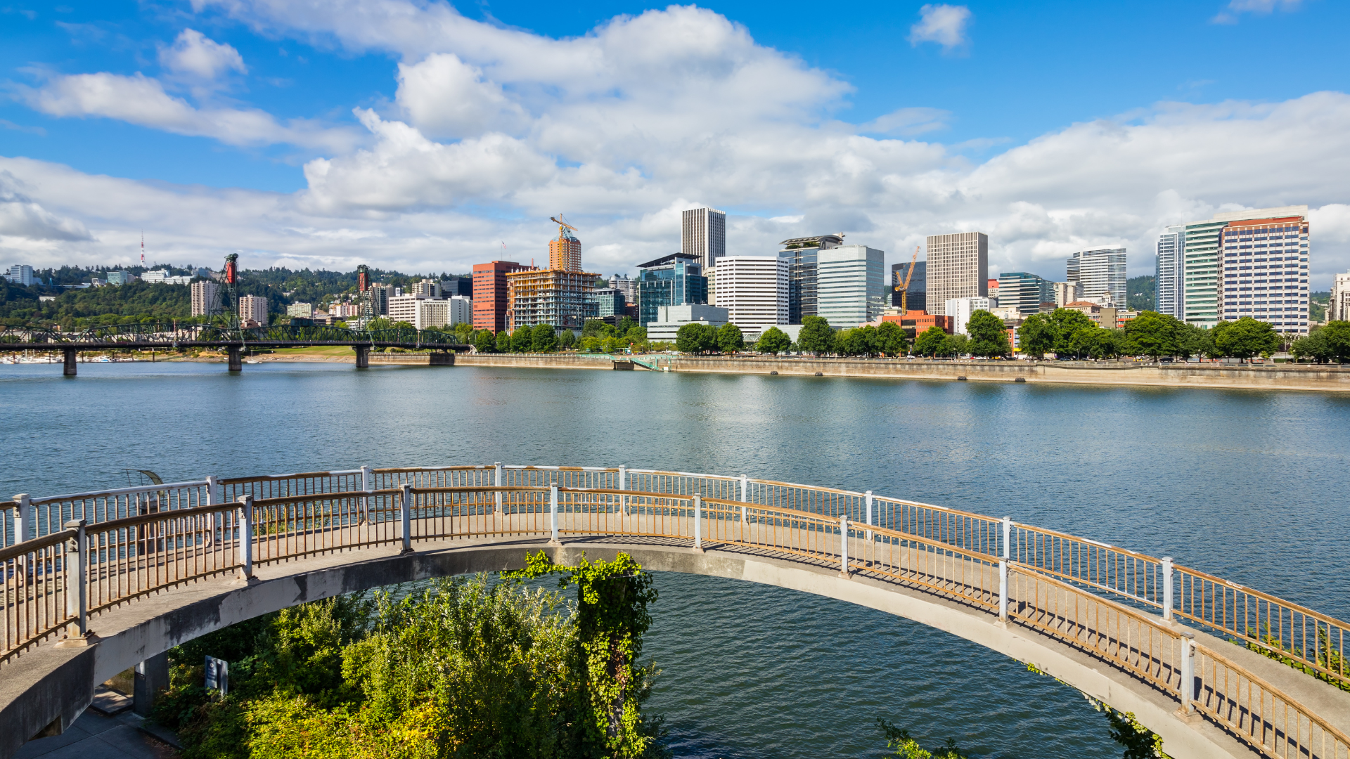 Portland, Oregon skyline over a river, seen from a walking bridge. Blue sky, sunny day.