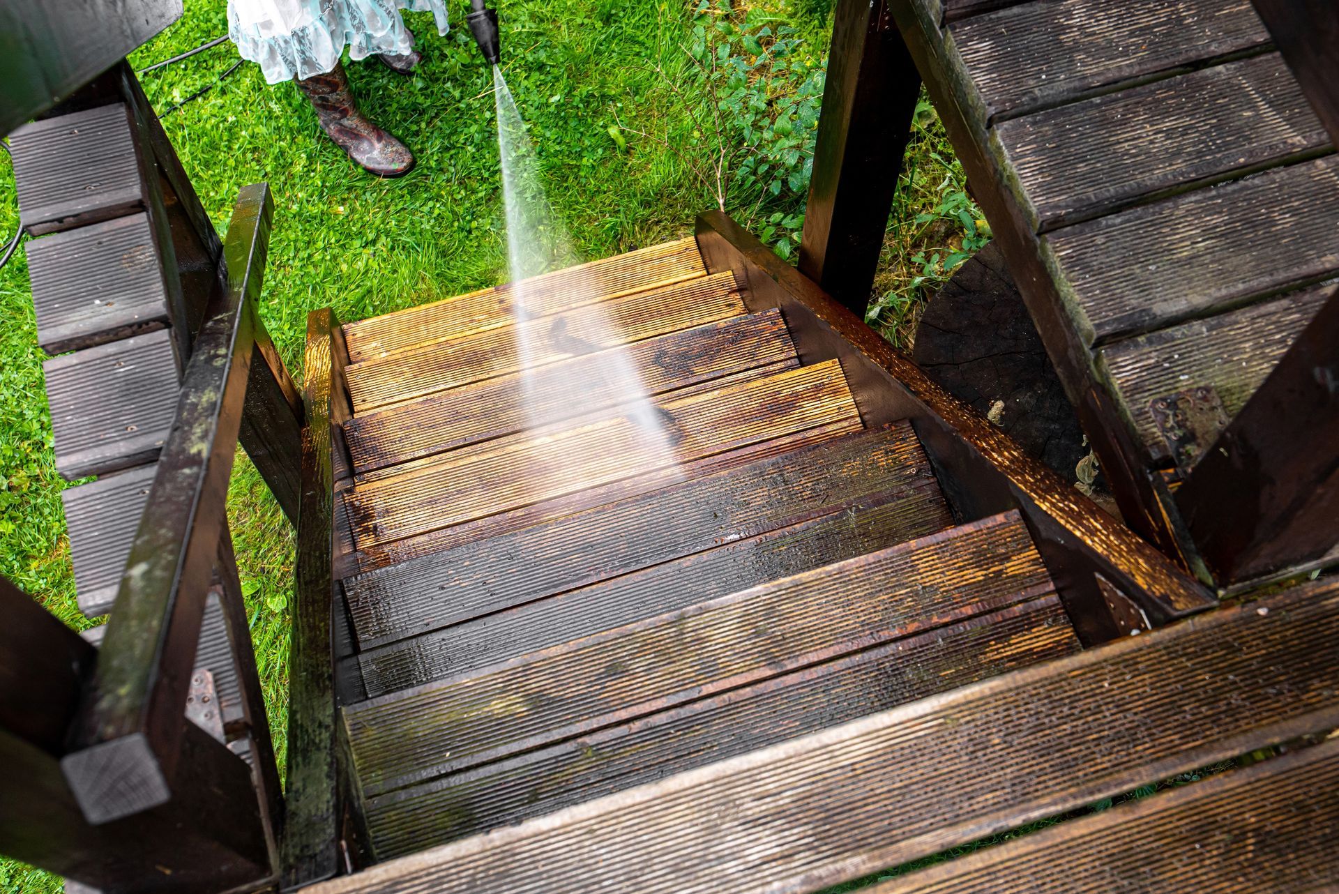 Person power washing wooden outdoor stairs with grass in the background.