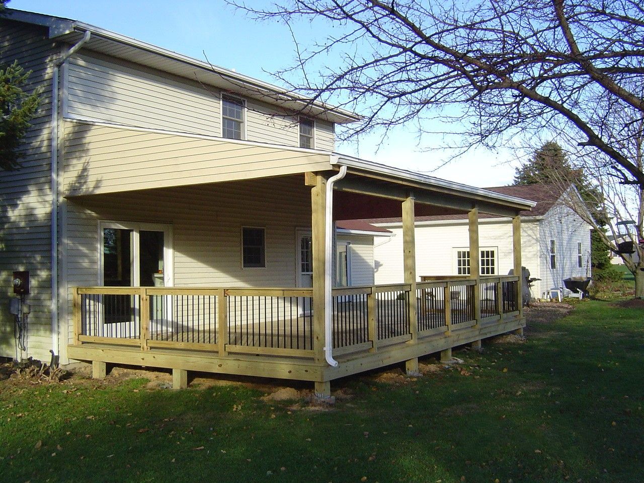 Yellow house with a wooden porch and railing, viewed from the yard under a leafy tree.