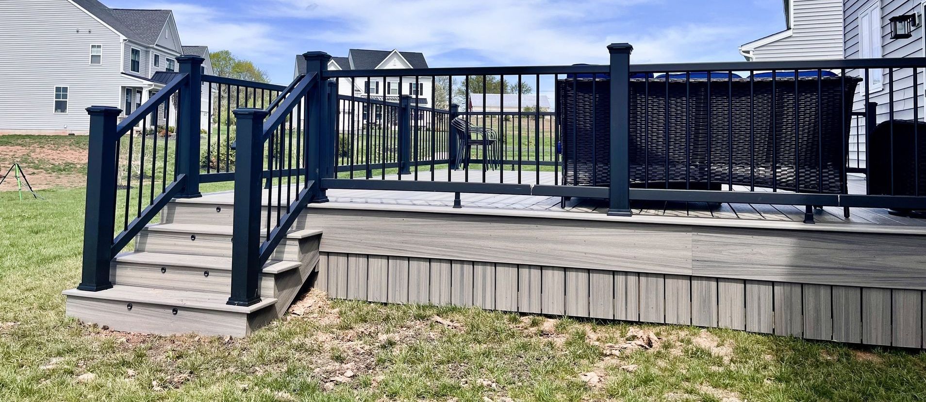 A deck with stairs and a black railing in the backyard of a house.